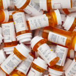 Dozens of prescription medicine bottles in a jumble. This collection of pill bottles is symbolic of the many medications senior adults and chronically ill people take.