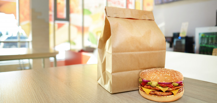 Cheeseburger and craft paper bag on wooden counter of cafe
