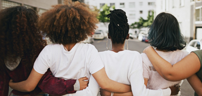 Rearview shot of a group of unrecognizable young friends walking with their arms around each other in the city