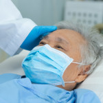 Doctor touching and checking Asian senior or elderly old lady woman patient wearing a face mask in hospital for protect infection and kill Novel Coronavirus Covid-19 virus