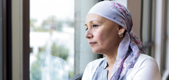 woman with cancer in head scarf looking out window