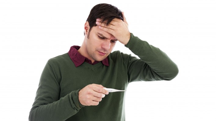 Young man holding his hand to his forehead and holding a thermometer