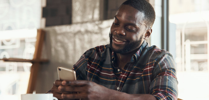 Shot of a handsome young man sitting and using his cellphone in a coffee shop during the day