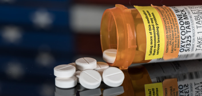 Prescription bottle for Oxycodone tablets and pills on wooden table with USA flag in background