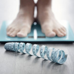 mans feet on scale with measuring tape on floor