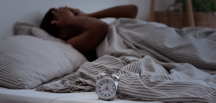 Sleepless, woman suffering from insomnia, sleep apnea or stress, headache or migraine. Tired and exhausted african american lady awake in middle of night, near alarm clock with time in dark, panorama
