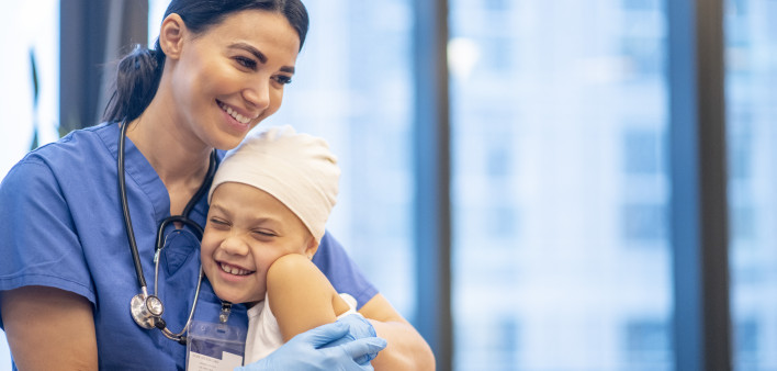 Nurse Hugging Young Cancer Patient stock photo A young Latin female nurse hugs her cancer patient as they enjoy a brief moment together. The young girl is smiling and happy. The nurse is wearing blue scrubs with a stethoscope around her neck, while the yo