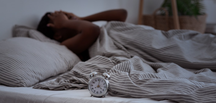Sleepless, woman suffering from insomnia, sleep apnea or stress, headache or migraine. Tired and exhausted african american lady awake in middle of night, near alarm clock with time in dark, panorama