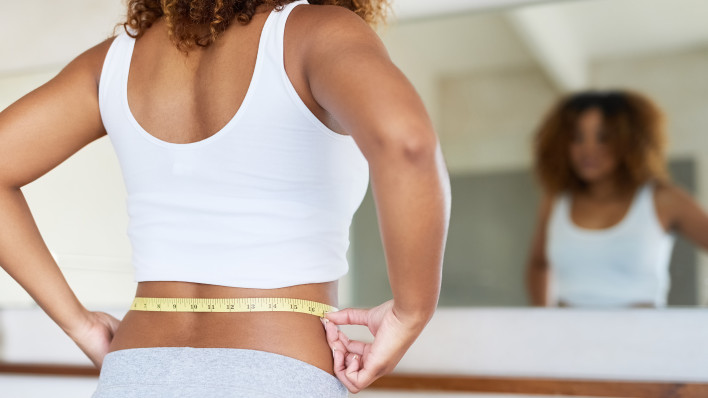 ropped shot of a young woman measuring her waist in the bathroom