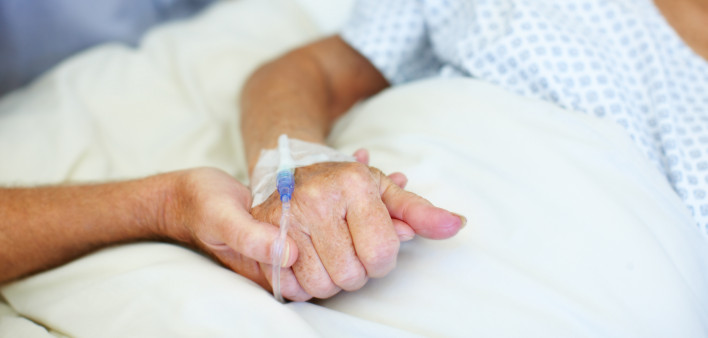 Closeup shot of an elderly man holding his wife's hand while she is ill in the hospital