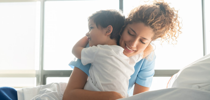 Beautiful sweet little boy hospitalized in the pediatrics ward hugging young nurse both smiling