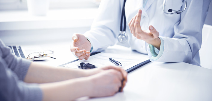 Doctor and female patient sitting at the desk and talking in clinic near window. Medicine and health care