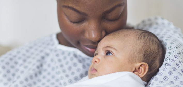 Beautiful African American mother in a hospital gown holds her newborn baby