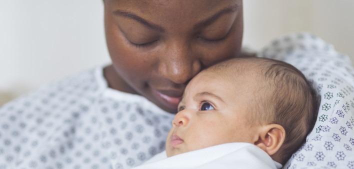 Beautiful African American mother in a hospital gown holds her newborn baby