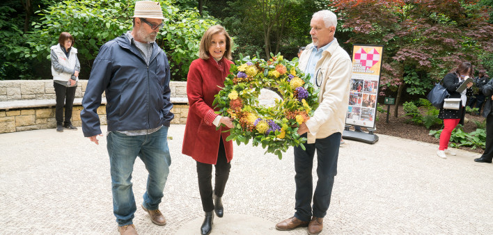 Speaker Emerita Nancy Pelosi displays the Grove Volunteer Workday Commemorative Wreath along with John Cunningham, CEO, National AIDS Memorial on the right, and Mike Shriver, former National AIDS Memorial board member and AIDS Activist, on the left.