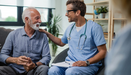 Happy doctor talking to senior male patient while being in a home visit.