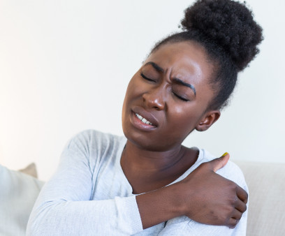 African woman sitting on couch take break touches her shoulder suffers from painful feelings ache caused by poor wrong posture, sedentary work, sitting at laptop for long period