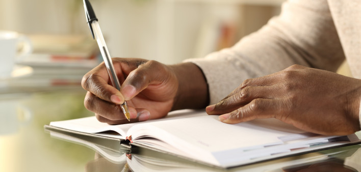 Close up of a black man hands writing reminder on paper agenda on a desk at home
