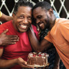 Three men laughing hugging birthday cake