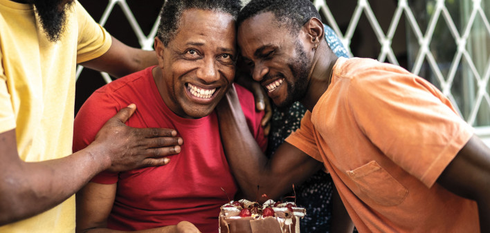 Three men laughing hugging birthday cake