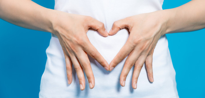 Young woman who makes a heart shape by hands on her stomach