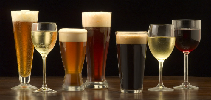 An assortment of glasses of wine and beer including a classic pilsner flute, a sparkling wine glass, an American half pint glass, a weizen or wheat beer glass, an American pint glass, a white wine glass, and a red wine glass.