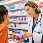Pharmacist giving medicine box to customer in pharmacy. Doctor showing and explaining medicine dose to customer. Mature pharmacist giving advice on medicaments, while serving young african woman.