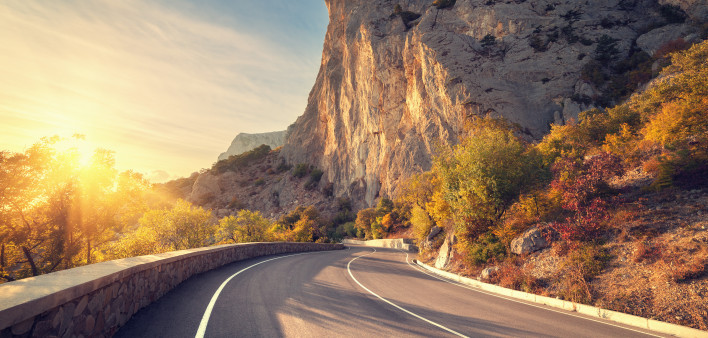 Asphalt road in autumn forest at sunrise. Crimean mountains