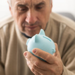 Senior caucasian man holding piggy bank with glasses depressed and worry for distress, crying angry and afraid.