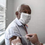 Nurse applying vaccine on patient's arm using face mask