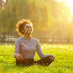 Happy young woman sitting outdoors in yoga position