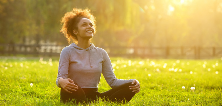 Happy young woman sitting outdoors in yoga position