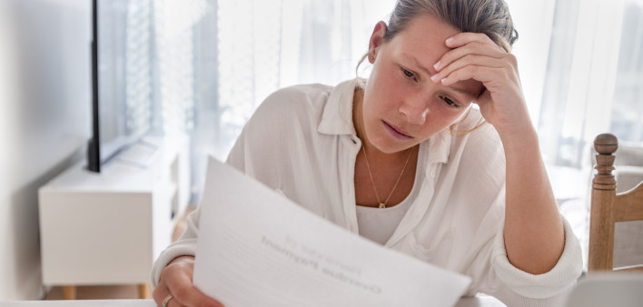 Woman looking worried holding paperwork at home. She is reading a financial bill or a letter with bad news. She looks very stressed and upset.