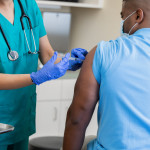 Nurse gives mature African American man a vaccination in doctor's office during coronavirus pandemic