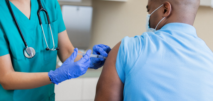 Nurse gives mature African American man a vaccination in doctor's office during coronavirus pandemic