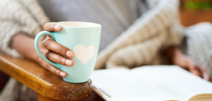 woman holding coffe cup with heart and heading a book