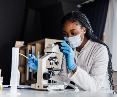female scienitst analyzing a sample under a microscope while doing research