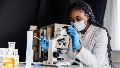female scienitst analyzing a sample under a microscope while doing research