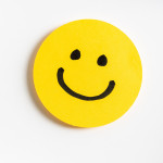 Drawing of a happy smiling emoticon on a yellow paper and white background.