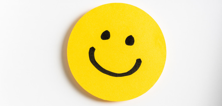 Drawing of a happy smiling emoticon on a yellow paper and white background.