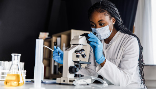 female scienitst analyzing a sample under a microscope while doing research