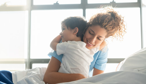 Beautiful sweet little boy hospitalized in the pediatrics ward hugging young nurse both smiling