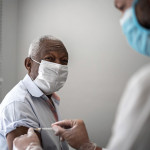 Nurse applying vaccine on patient's arm using face mask