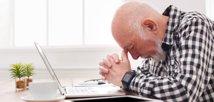 Worried senior man using laptop at home.