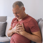 Severe heartache, man suffering from chest pain, having heart attack or painful cramps, pressing on chest with painful expression. Photo of Mature man suffering from chest pain at home during the day.