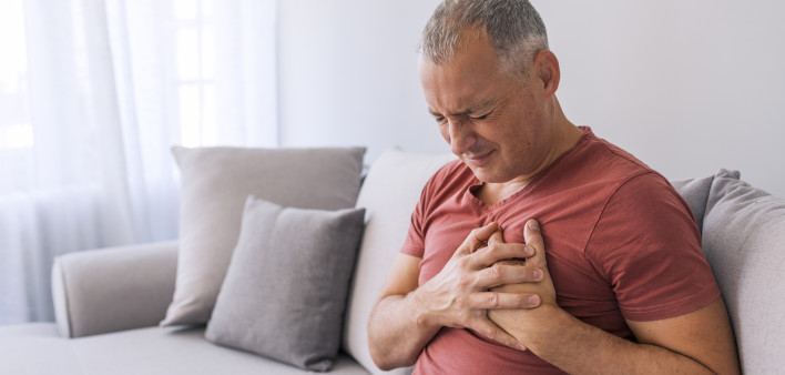 Severe heartache, man suffering from chest pain, having heart attack or painful cramps, pressing on chest with painful expression. Photo of Mature man suffering from chest pain at home during the day.
