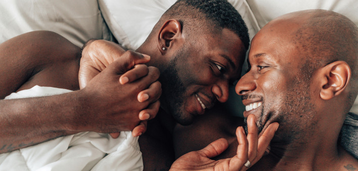 two black gay men holding hands and smiling in bed