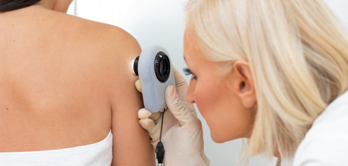 Female dermatologist examining female patient's skin with dermascope, doctor is carefully looking for signs of skin cancer