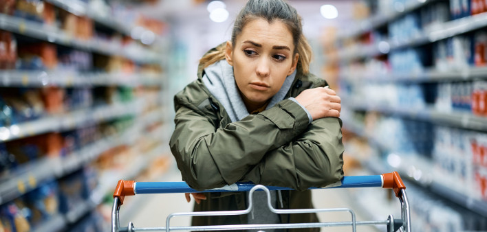 Young woman buying in supermarket and feeling worried about increase in food prices.