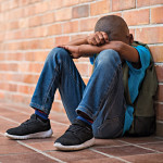 black boy sitting on floor hands in arms sad